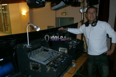 Un DJ mixe derrière une table éclairée de lumières LED violettes, avec un mur décoratif en arrière-plan.