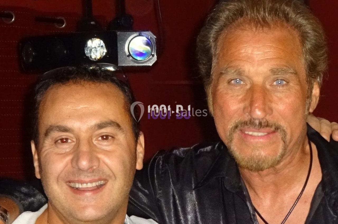 Deux hommes posant ensemble devant un fond rouge avec un projecteur visible en arrière-plan.