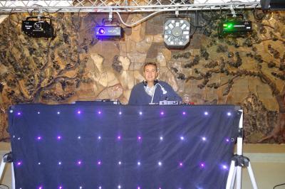 Un DJ mixe derrière une table éclairée de lumières LED violettes, avec un mur décoratif en arrière-plan.