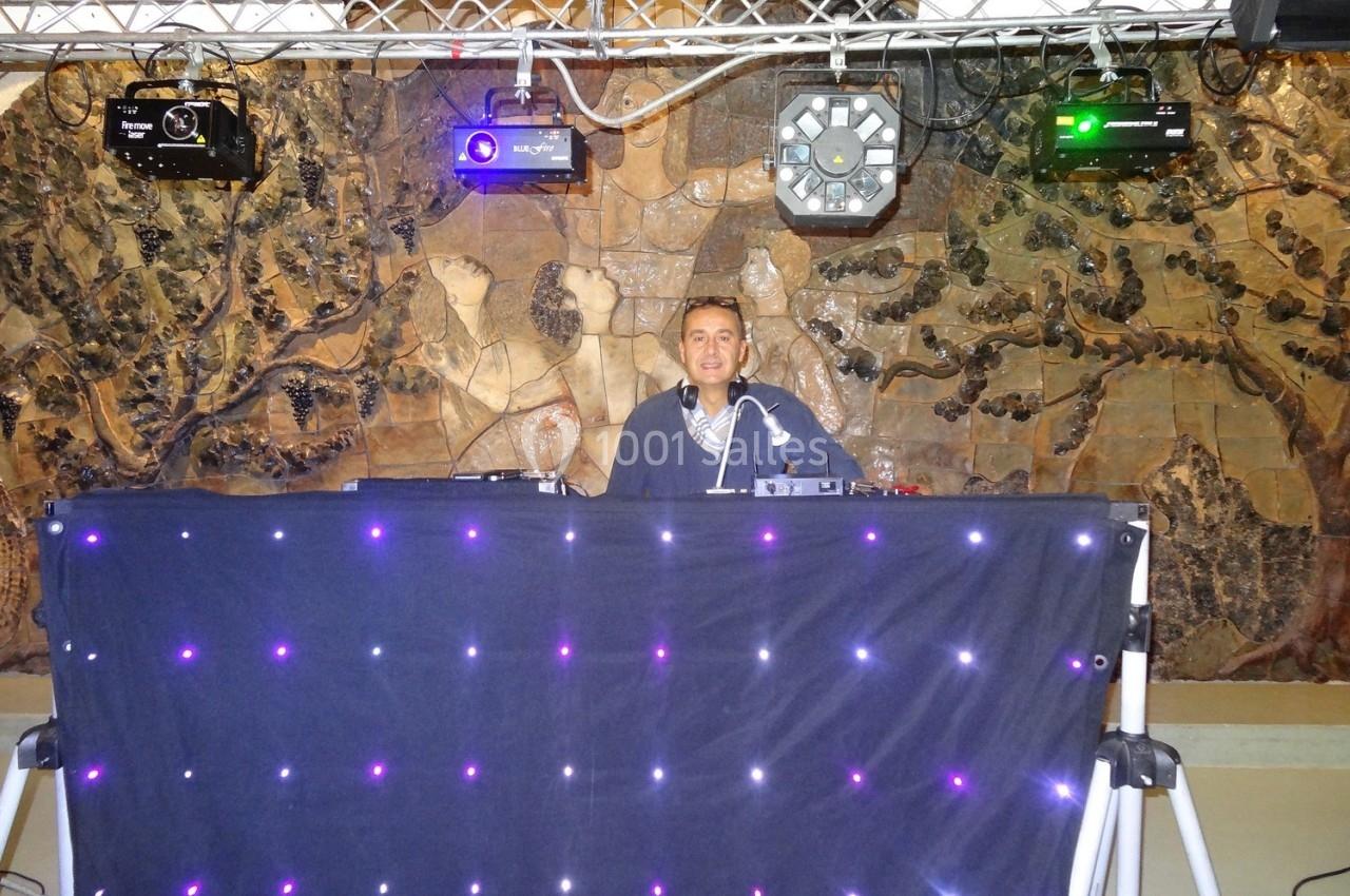 Un DJ mixe derrière une table éclairée de lumières LED violettes, avec un mur décoratif en arrière-plan.