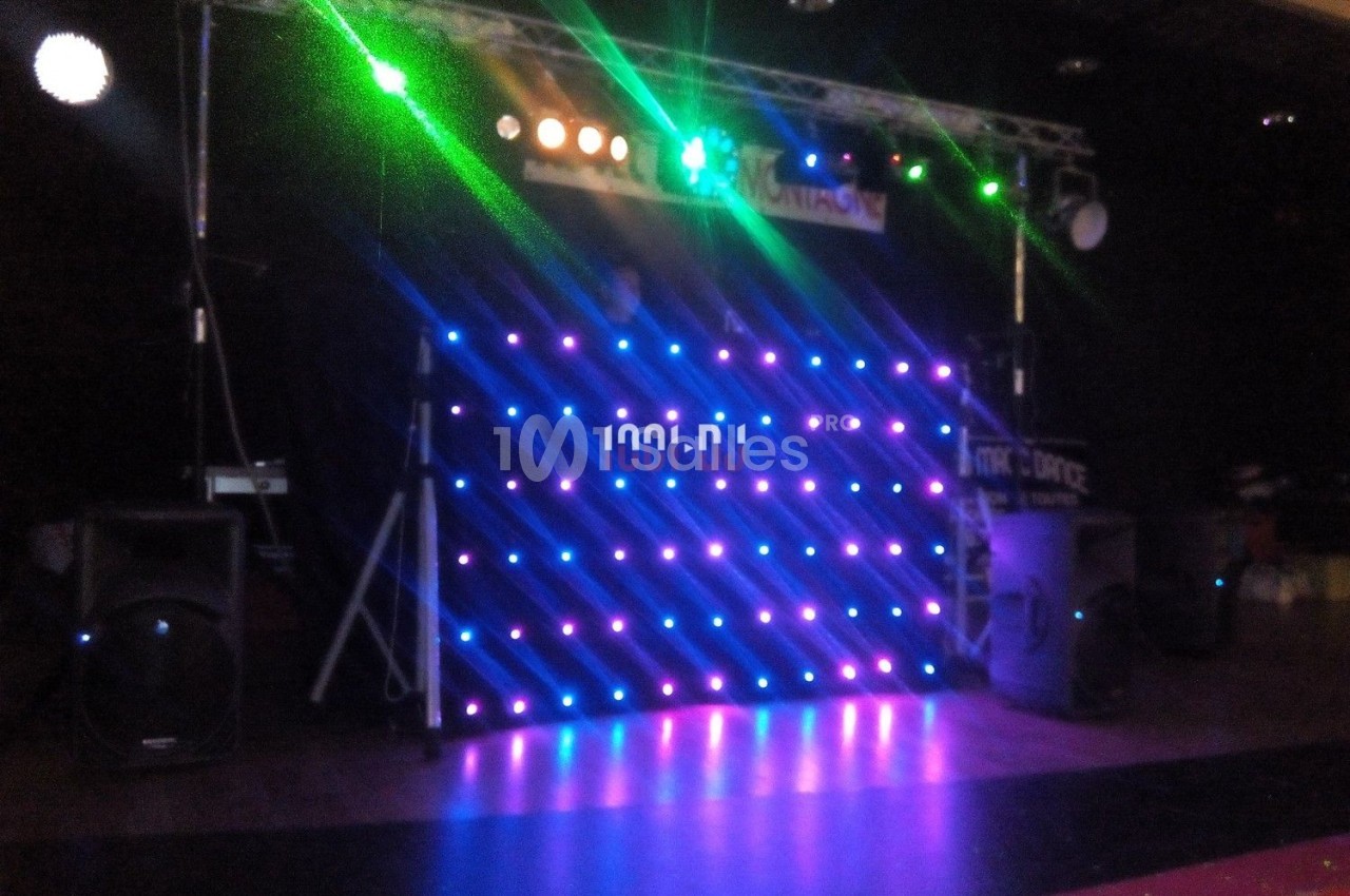 Pupitre de DJ illuminé par des lumières LED colorées, entouré d'équipements audio dans une salle sombre.