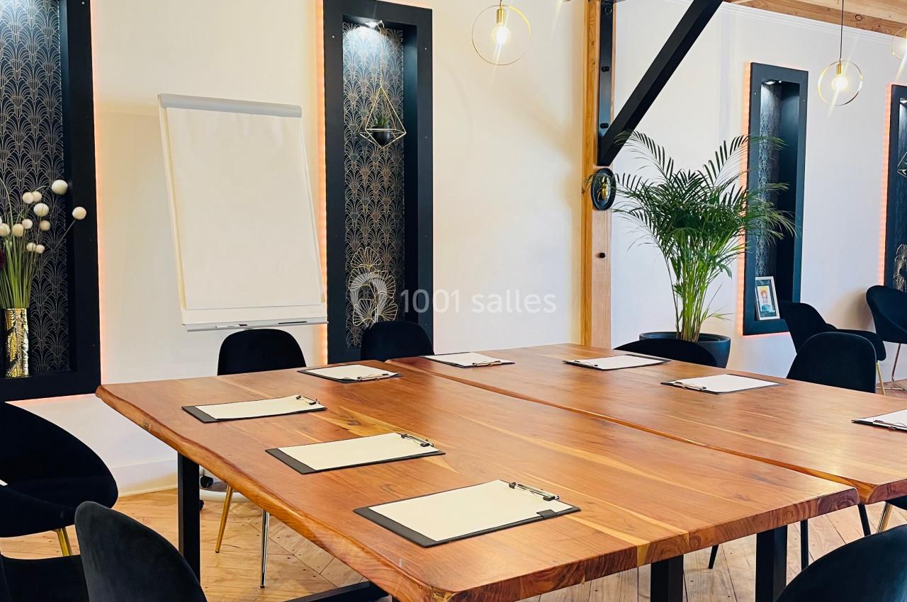 Salle de réunion lumineuse avec table en bois, chaises noires, paperboard et décoration végétale.
