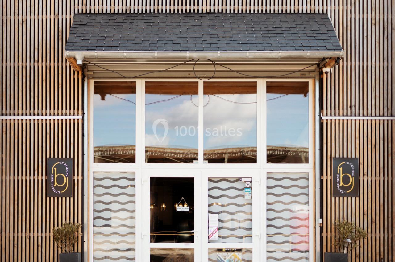 Façade d'un bâtiment avec une porte vitrée encadrée de bois et deux panneaux noirs portant un logo doré.