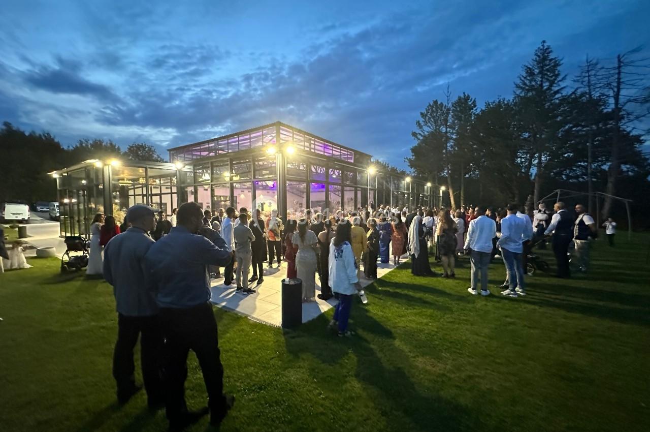 Groupe de personnes rassemblées en soirée devant un bâtiment vitré illuminé, entouré d'une pelouse et d'arbres.