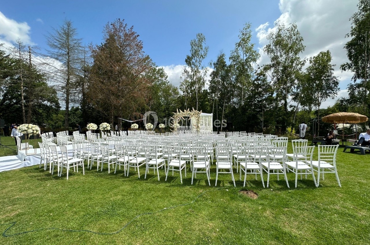 Chaises blanches alignées en extérieur sur une pelouse, face à une arche décorée pour une cérémonie en plein air.