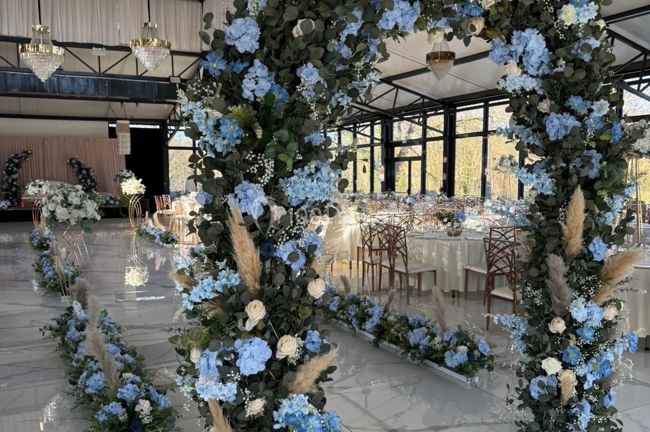 Décoration florale avec des arches ornées de fleurs bleues et blanches dans une salle de réception lumineuse.