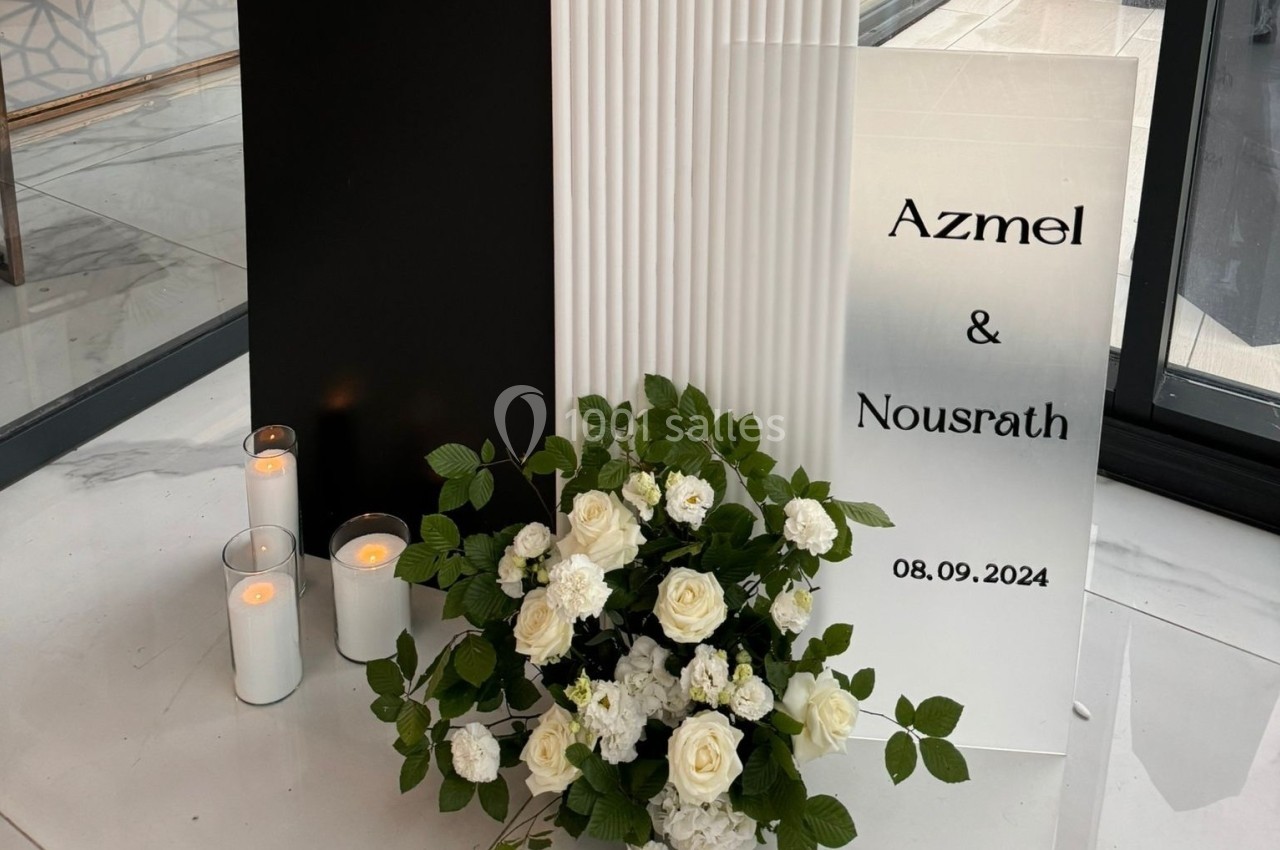 Panneau avec les prénoms ’Azmel & Nousrath’ et la date ’08.09.2024’, accompagné de bougies et d'un bouquet de roses blanches.