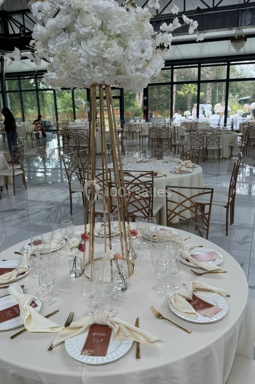 Table de réception élégamment dressée avec nappes blanches, couverts dorés et centre de table floral blanc.