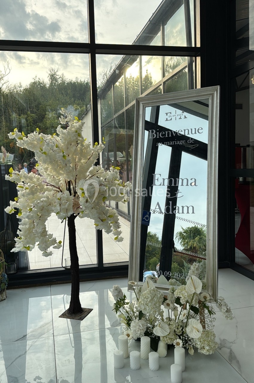 Panneau de bienvenue pour un mariage, avec un miroir encadré, des fleurs blanches et des bougies décoratives.