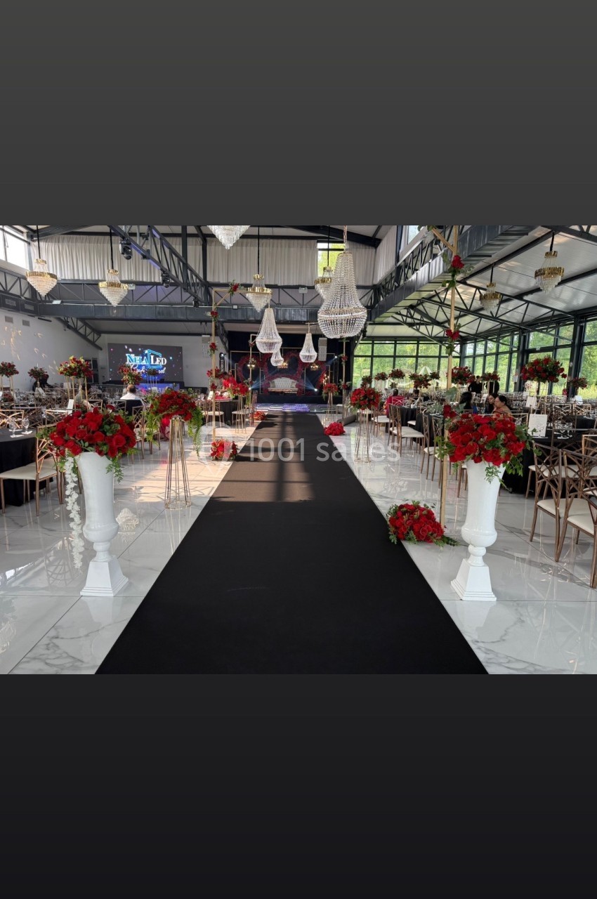 Allée centrale décorée de fleurs rouges et blanches dans une salle de réception spacieuse avec lustres suspendus.