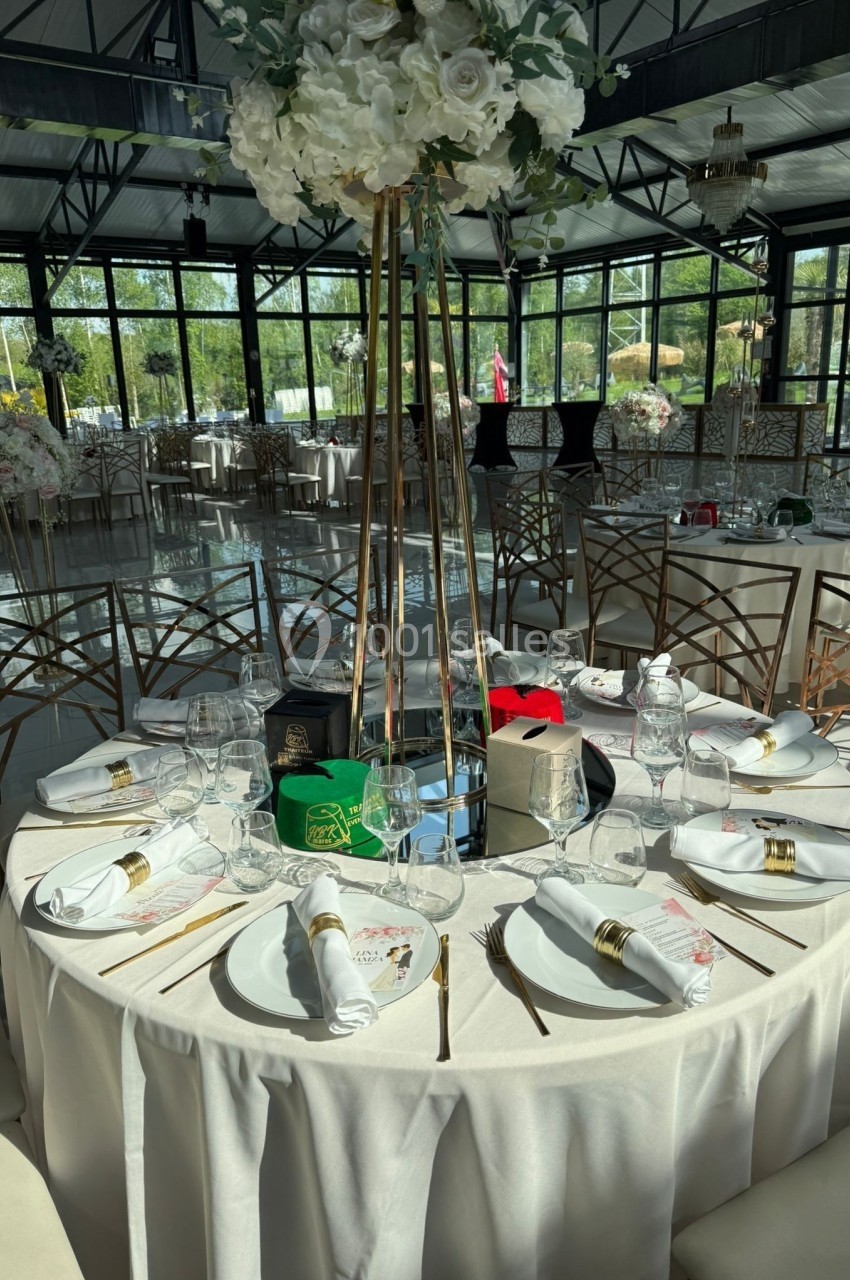 Table élégamment dressée avec nappes blanches, vaisselle raffinée, décor floral et lumière naturelle dans une salle de…