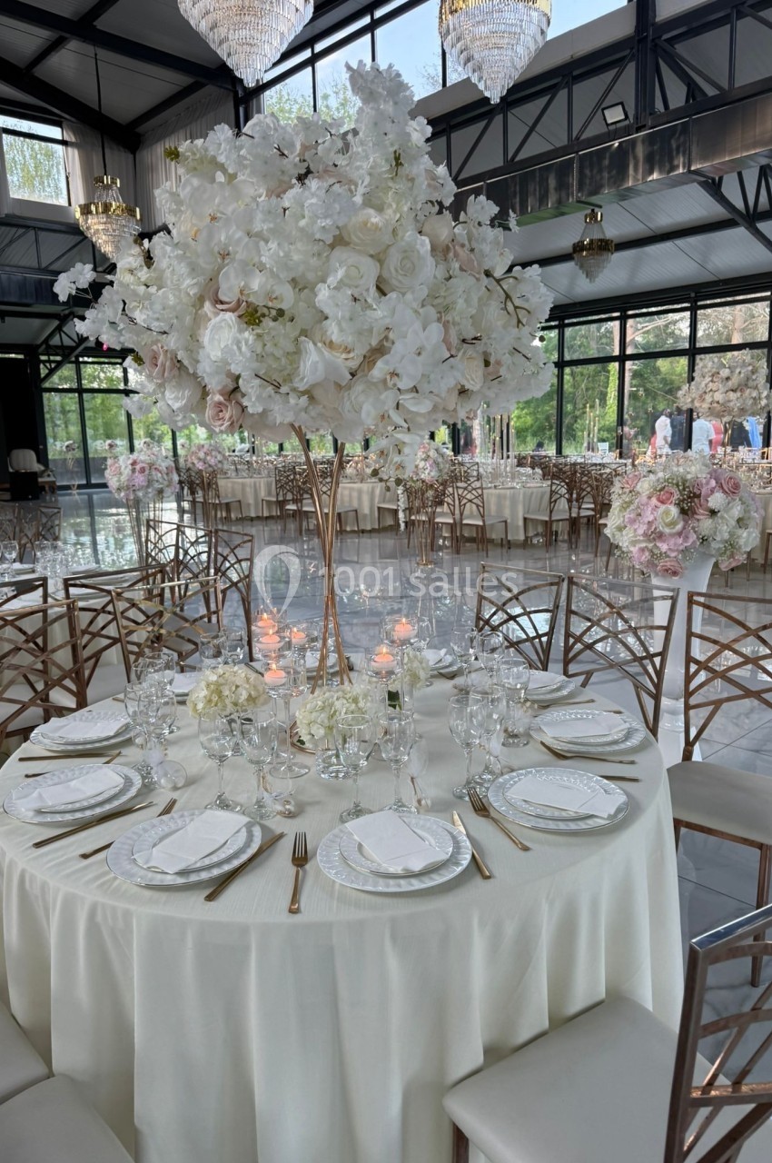 Table élégamment dressée avec une nappe blanche, vaisselle raffinée et un grand centre de table floral blanc et rose.
