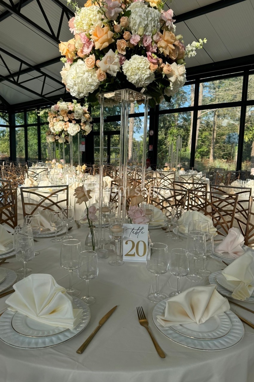 Salle de réception lumineuse avec une table décorée de fleurs pastel, nappes blanches et vaisselle élégante.