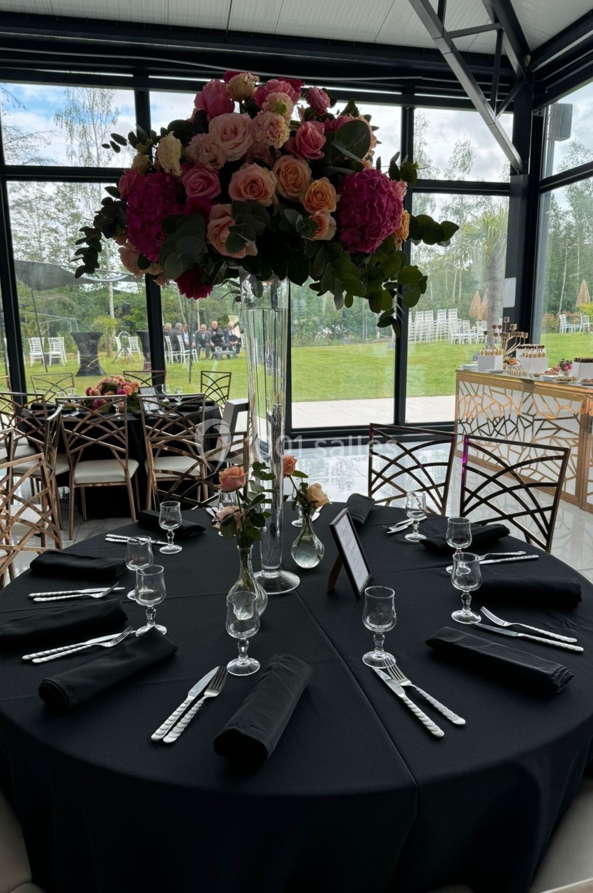 Table dressée avec une nappe noire, couverts disposés, et un grand bouquet de fleurs colorées en centre de table.