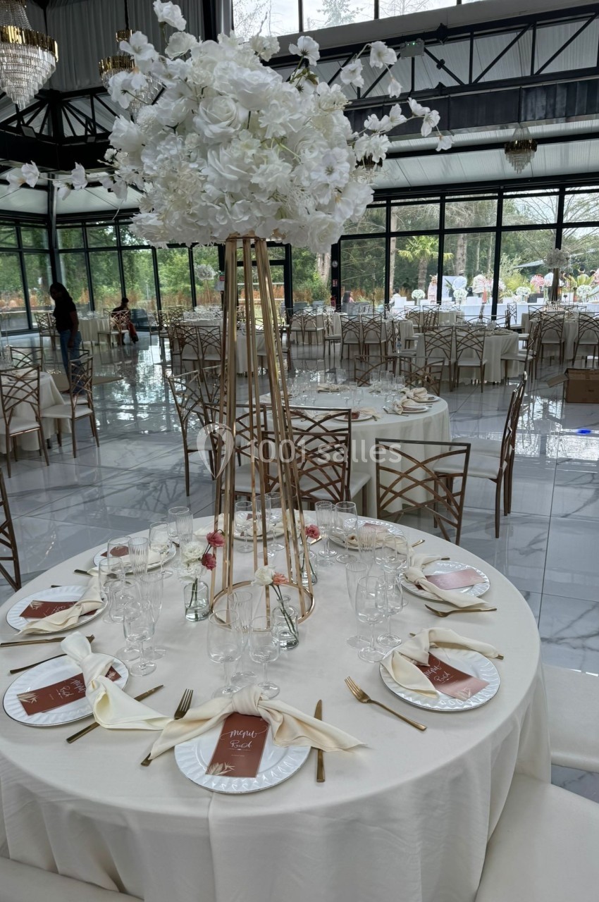 Salle de réception élégante avec tables rondes dressées, décorées de centres de table floraux blancs et couverts dorés.