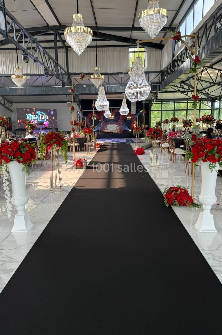 Salle de réception décorée avec des lustres, des fleurs rouges et blanches, et une allée centrale noire.