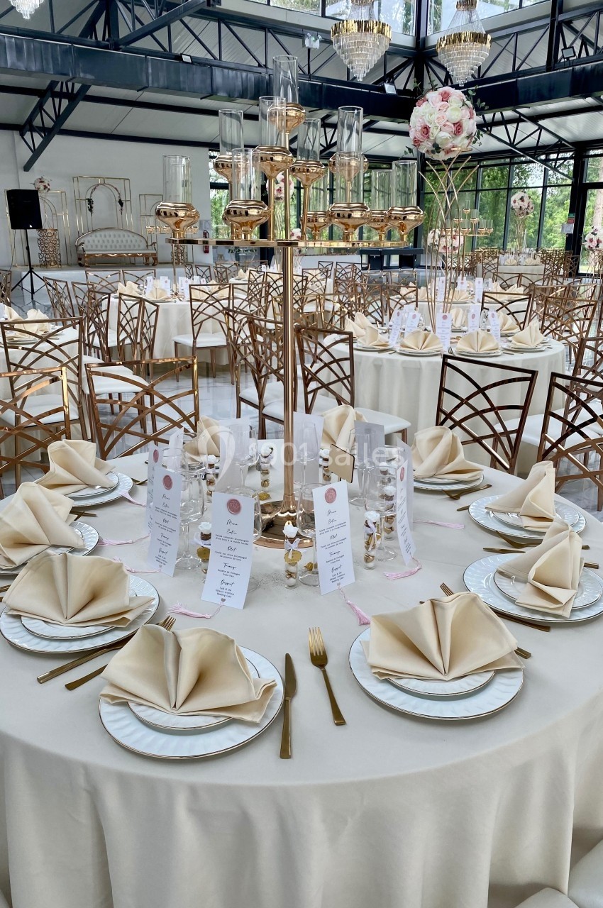 Table élégamment dressée avec nappes blanches, serviettes pliées, vaisselle raffinée et décorations dorées dans une salle…