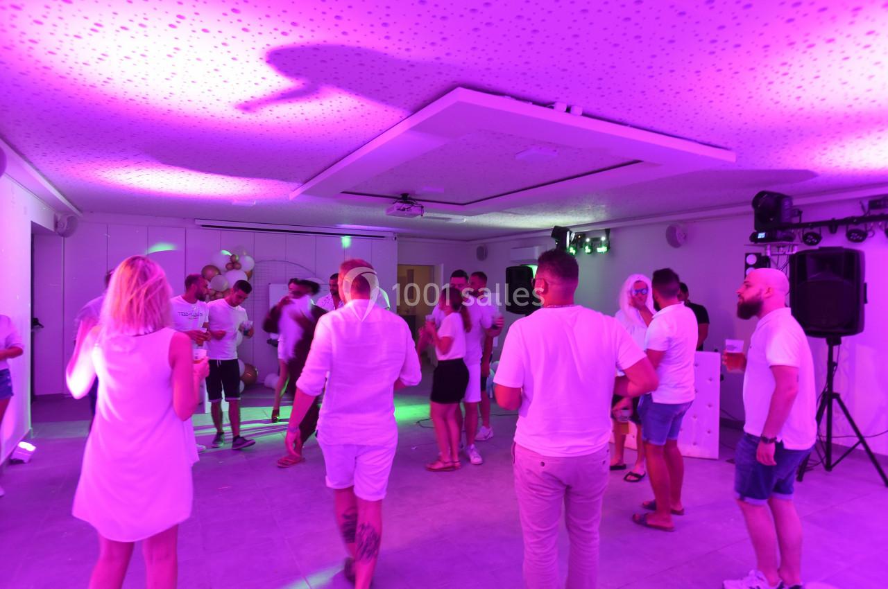Des personnes dansent et discutent dans une salle éclairée par des lumières violettes, lors d'un événement festif.