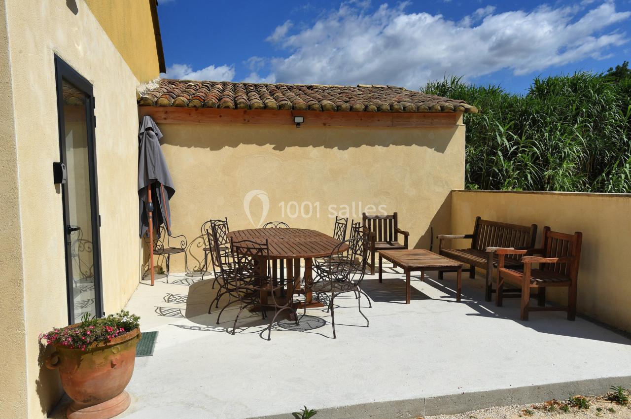 Terrasse ensoleillée avec mobilier de jardin en bois et métal, adossée à une maison aux murs clairs.