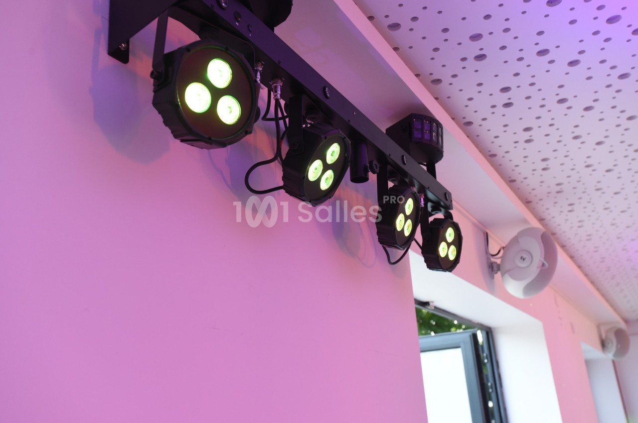Projecteurs LED suspendus émettant une lumière colorée dans une pièce avec un plafond perforé.