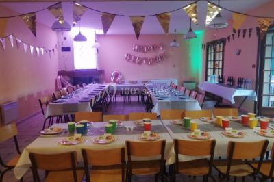 Des personnes assises en extérieur assistent à une cérémonie devant des tables décorées, près de chalets en bois.