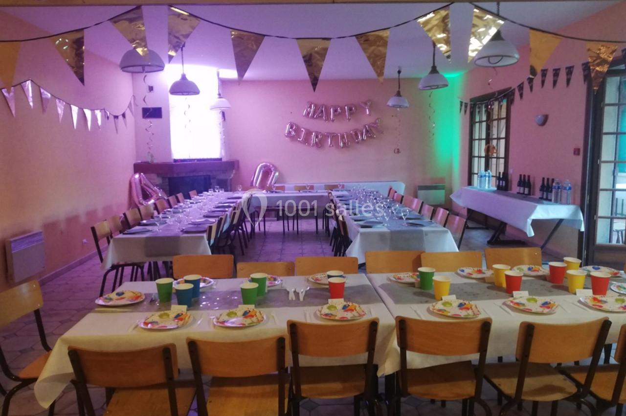 Salle décorée pour un anniversaire avec tables dressées, chaises alignées, guirlandes et ballons en arrière-plan.