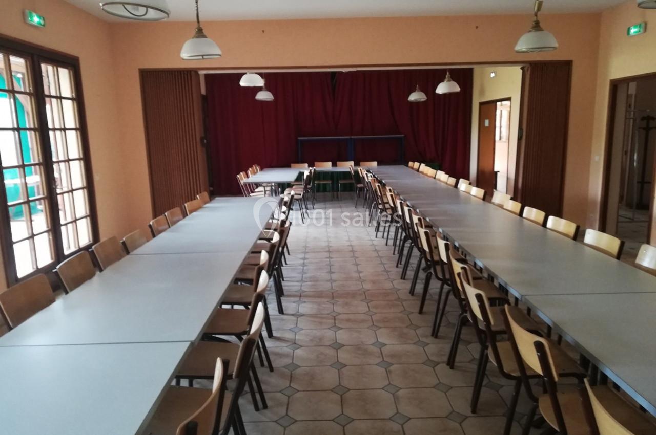 Salle de réunion avec de longues tables alignées, des chaises en bois et un rideau rouge en fond.