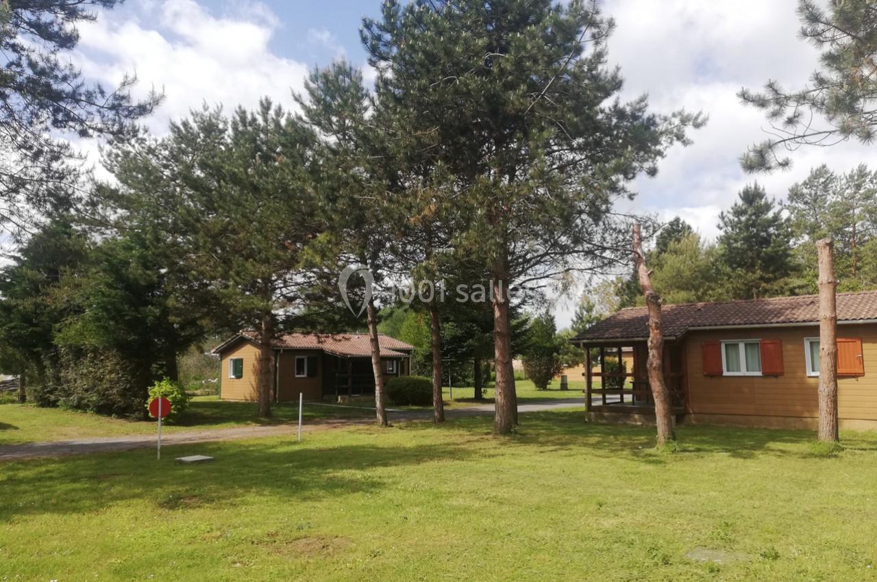Chalets en bois entourés d'arbres dans un espace vert sous un ciel partiellement nuageux.