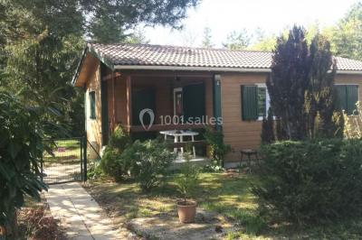 Des personnes assises en extérieur assistent à une cérémonie devant des tables décorées, près de chalets en bois.