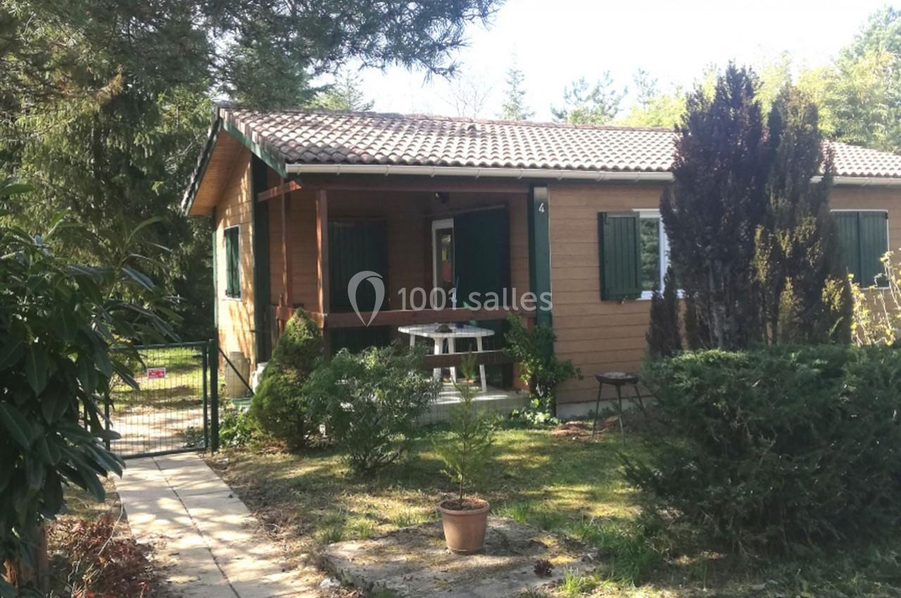 Maison en bois avec terrasse, entourée de végétation et située dans un jardin arboré sous un ciel clair.