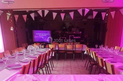 Des personnes assises en extérieur assistent à une cérémonie devant des tables décorées, près de chalets en bois.