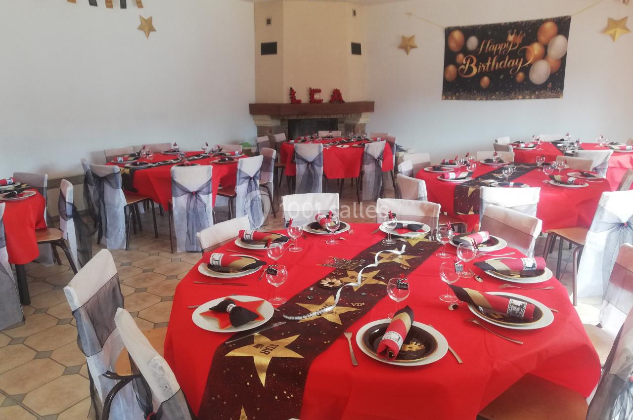 Salle décorée pour un anniversaire avec des tables dressées en rouge et noir, ornées de nappes et serviettes assorties.