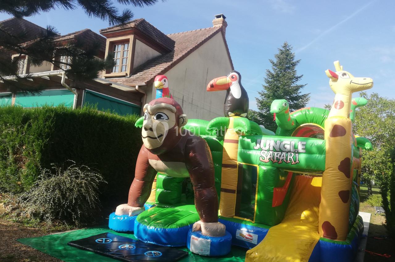 Structure gonflable colorée sur le thème de la jungle avec un singe, des toucans et une girafe, installée en extérieur.