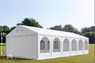 Des personnes assises en extérieur assistent à une cérémonie devant des tables décorées, près de chalets en bois.