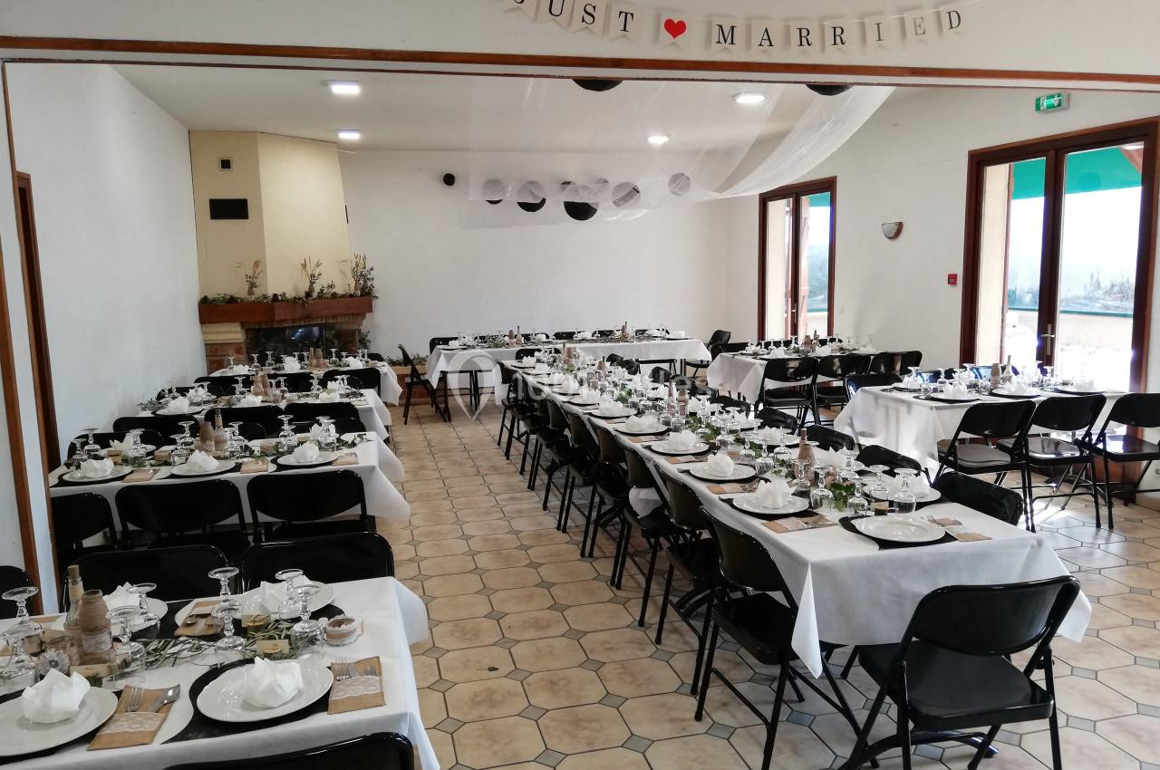 Salle décorée pour un mariage avec des tables alignées, nappes blanches, vaisselle disposée et une bannière ’Just Married’.