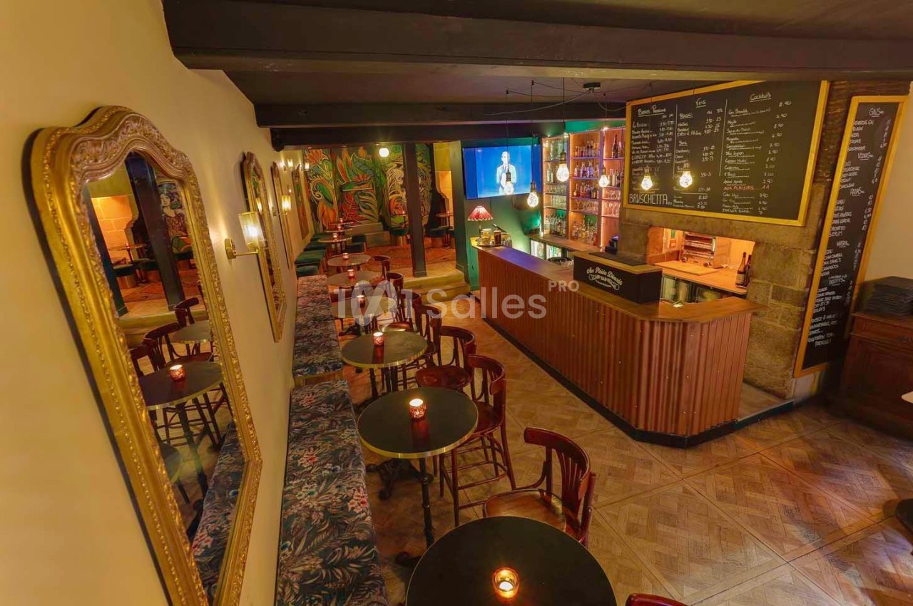 Intérieur d'un bar chaleureux avec tables rondes, bougies, grand miroir, comptoir en bois et menu affiché au mur.