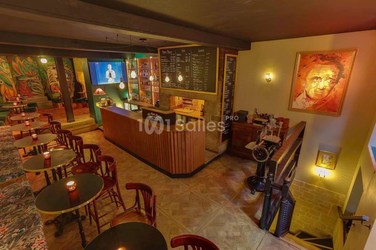 Intérieur d'un bar chaleureux avec comptoir en bois, tables rondes, éclairage tamisé et décorations artistiques.