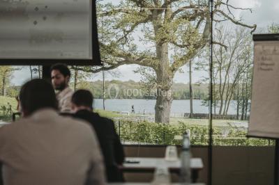 Miniature Natura Parc #10 Groupe de personnes rassemblées devant une maison en pierre avec un chapiteau, sur une pelouse par temps ensoleillé.