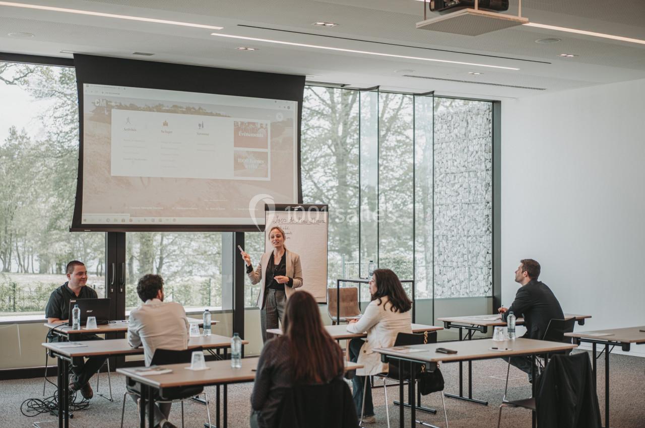 Photo Natura Parc #11 Une femme présente devant un écran et un tableau lors d'une réunion dans une salle lumineuse avec plusieurs participants.