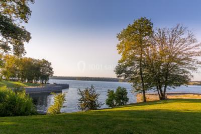 Miniature Natura Parc #13 Groupe de personnes rassemblées devant une maison en pierre avec un chapiteau, sur une pelouse par temps ensoleillé.