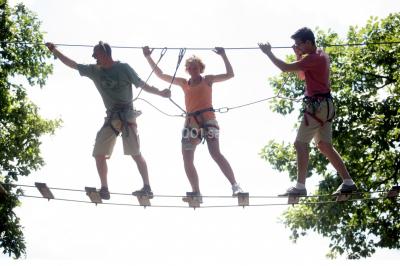 Miniature Natura Parc #3 Groupe de personnes rassemblées devant une maison en pierre avec un chapiteau, sur une pelouse par temps ensoleillé.