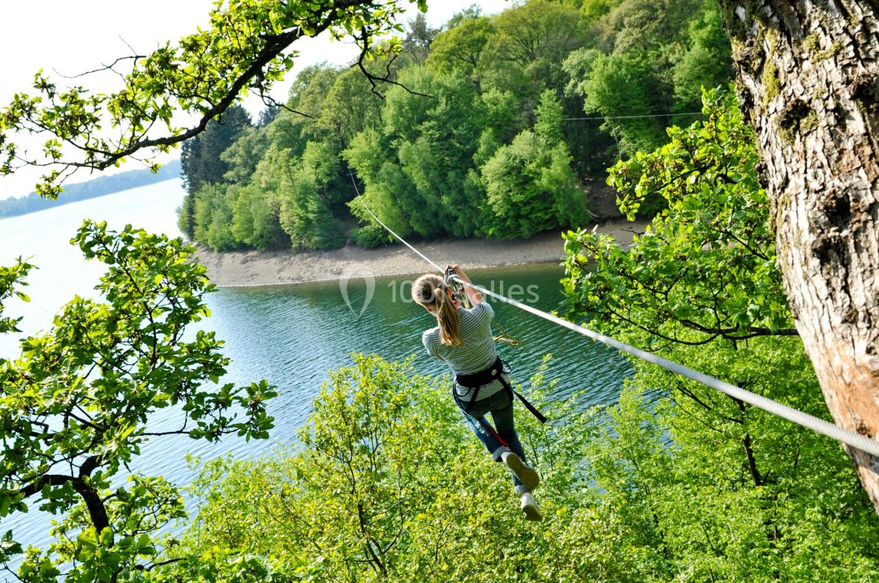 Photo Natura Parc #7 Une personne traverse un lac sur une tyrolienne entourée de forêt verdoyante.