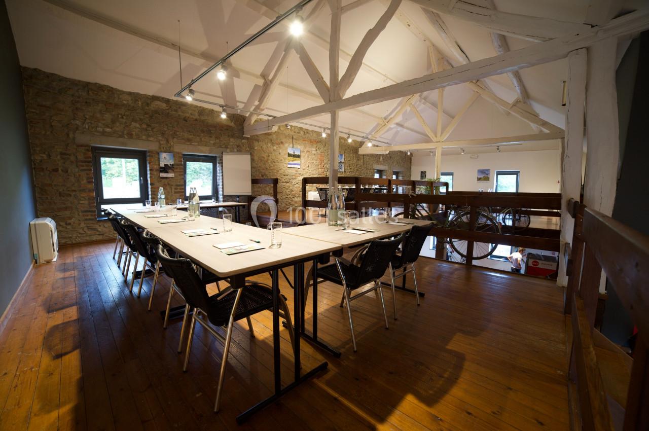 Photo Natura Parc #22 Salle de réunion lumineuse avec poutres apparentes, tables alignées, chaises noires et vue sur l'extérieur par de grandes…