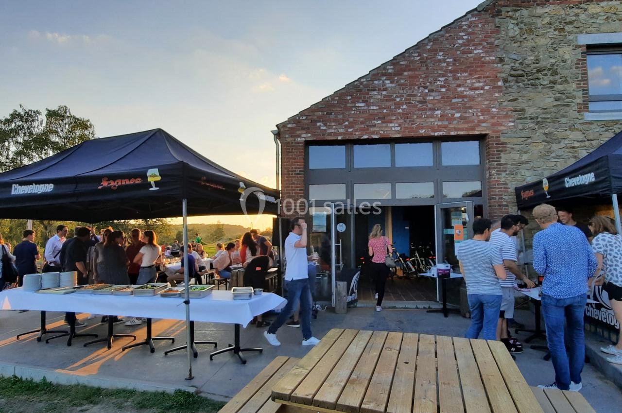 Photo Natura Parc #24 Groupe de personnes réunies en extérieur près d'un bâtiment en pierre, avec des stands sous des tentes noires.