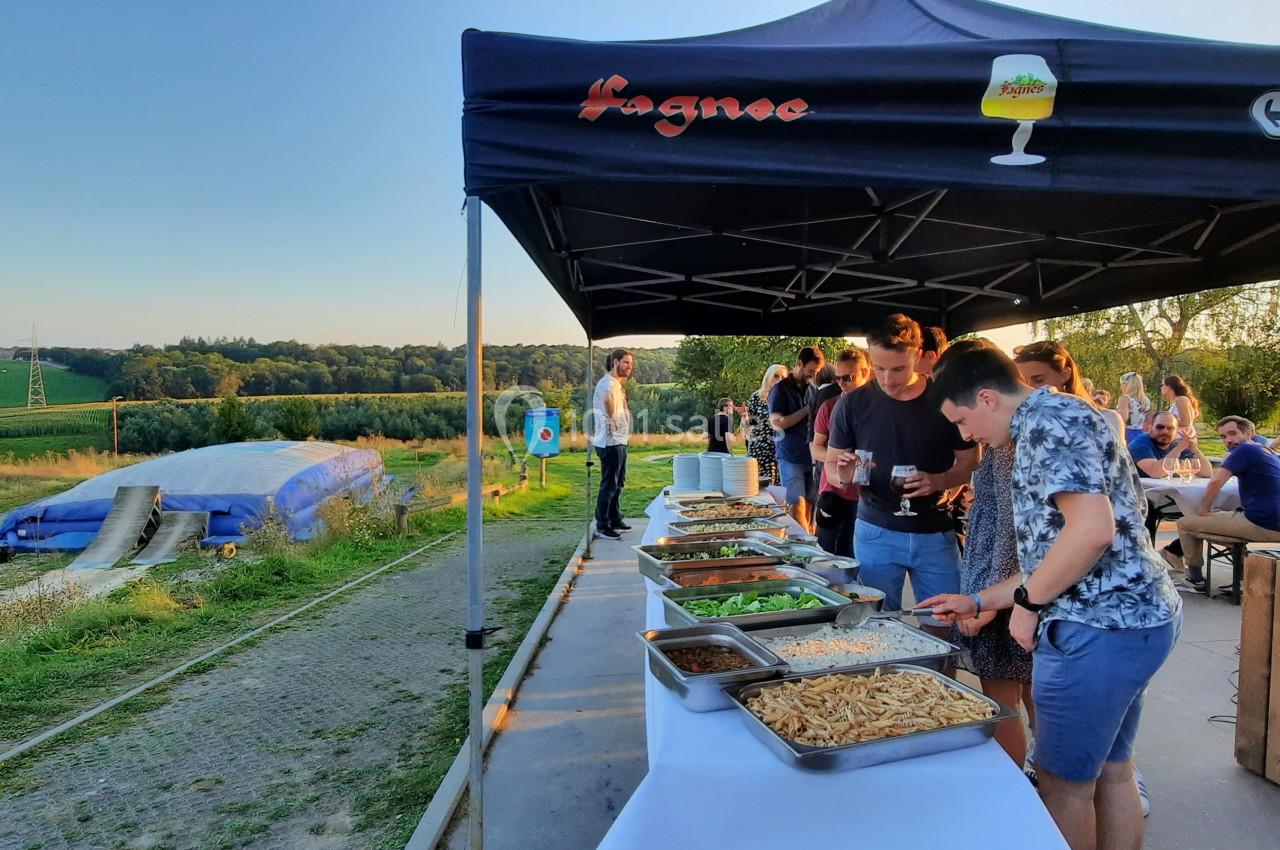 Photo Natura Parc #25 Des personnes se servent à un buffet en plein air sous une tente, avec un paysage champêtre en arrière-plan.