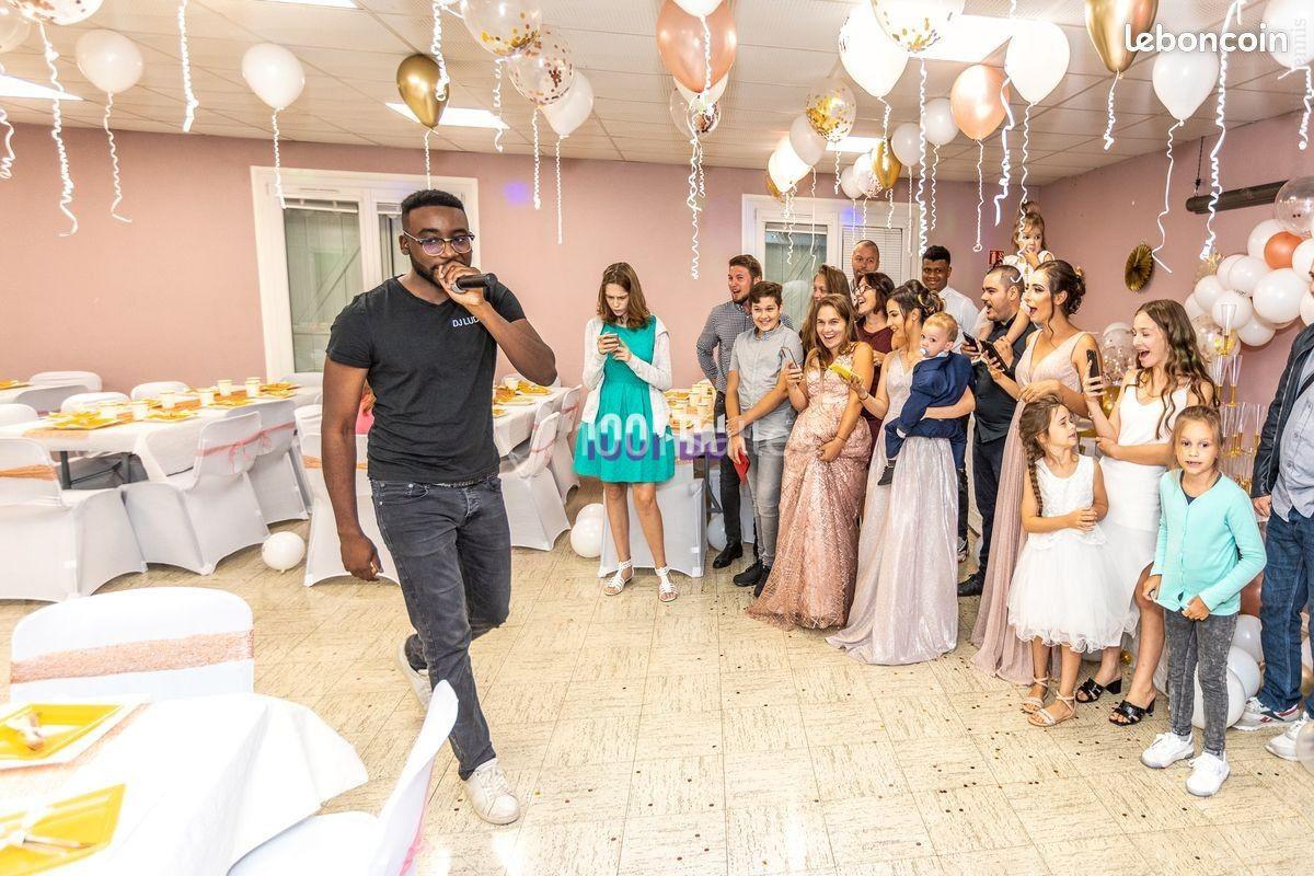 Un homme chante au micro dans une salle décorée pour une fête, entouré d'invités attentifs et souriants.