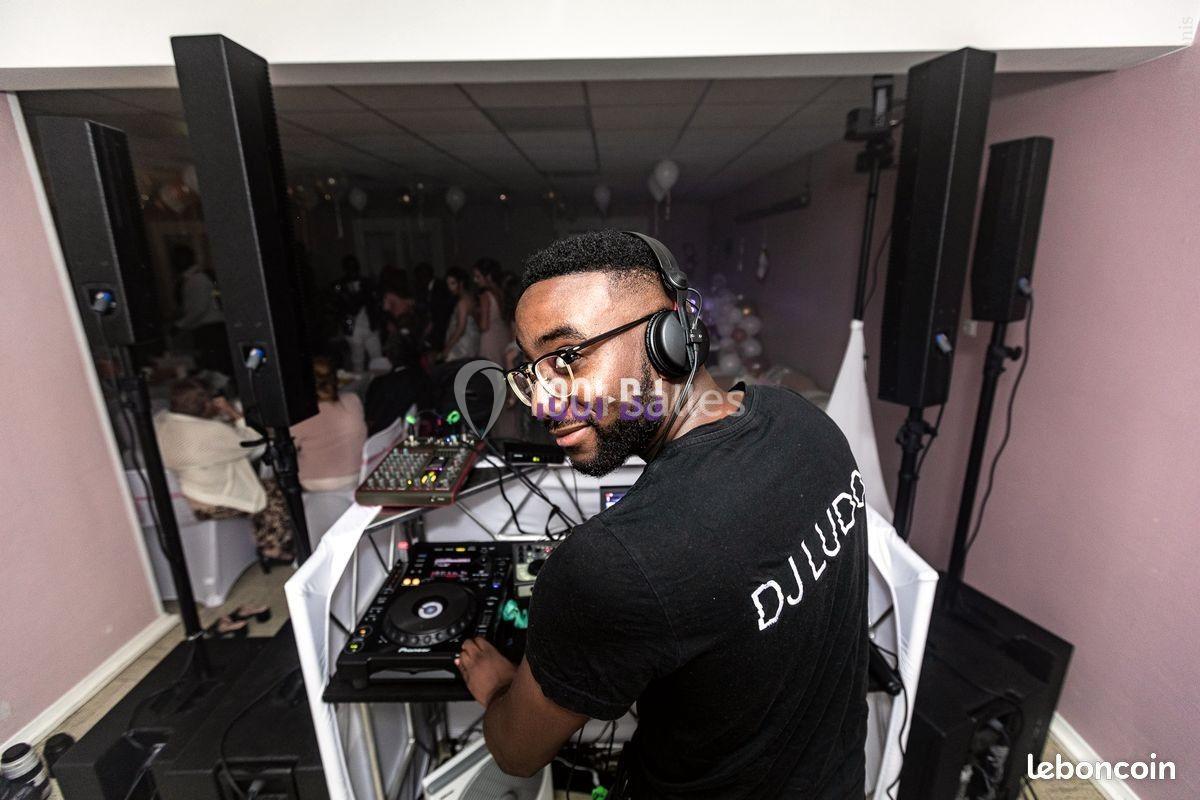 Un DJ mixe de la musique sur une table de mixage dans une salle éclairée, entouré d'équipements audio.