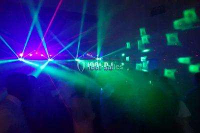 Salle sombre avec des jeux de lumières colorées, des lasers et une foule dans une ambiance festive.