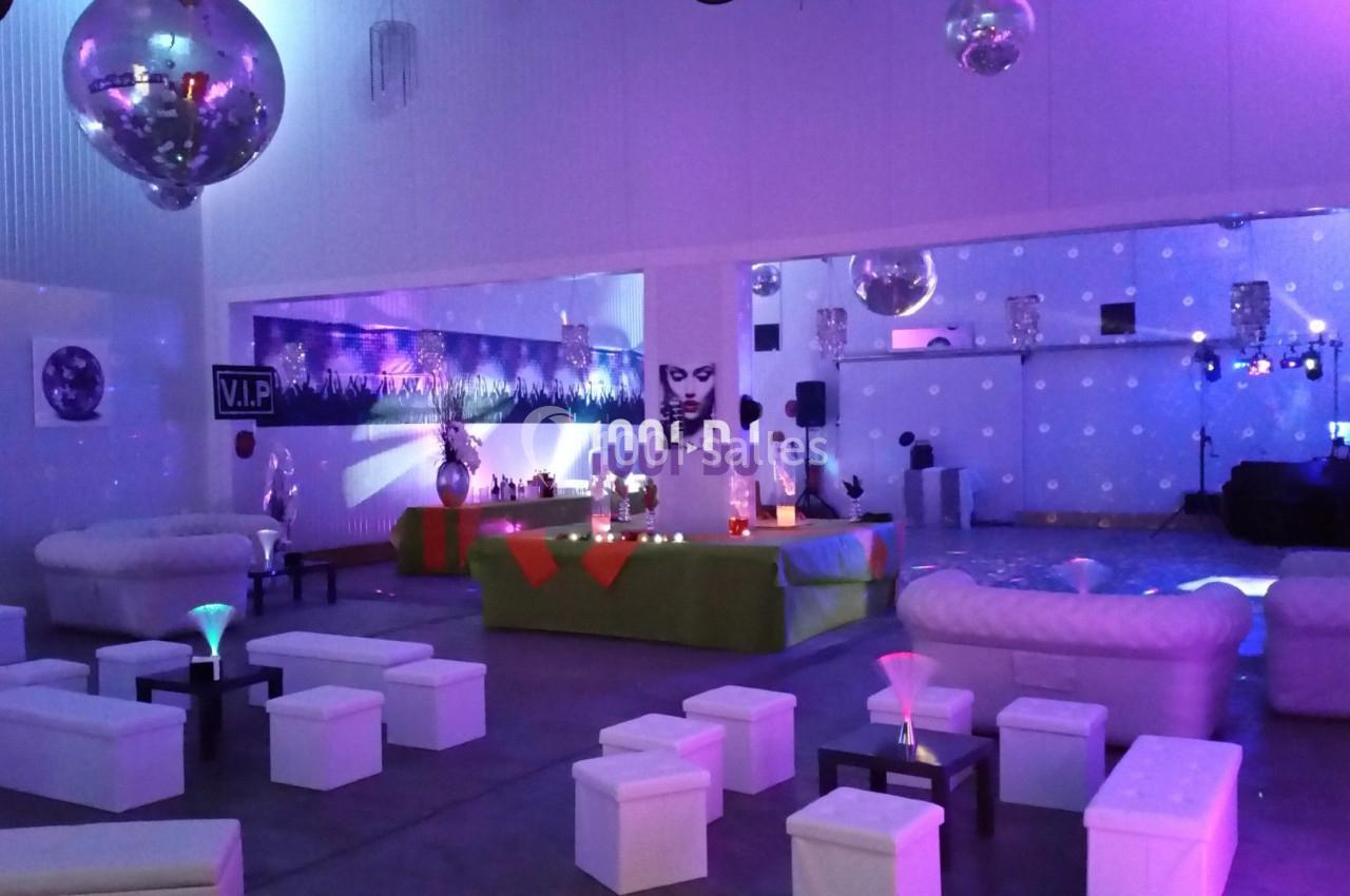 Salle décorée pour un événement, avec canapés blancs, tables basses, éclairage coloré et ambiance festive.