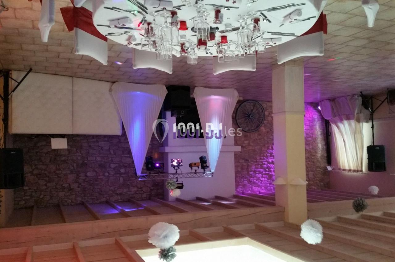 Salle de réception décorée avec des tables dressées, éclairages colorés et espace DJ en arrière-plan.